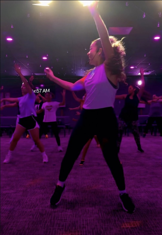 An Enough7Fitness cardio dance class mid-song, arms up under purple lights